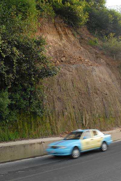 Eroding hill along a roadside with a cab speeding by.