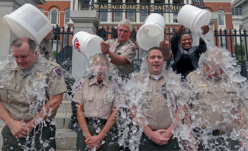 Photograph of four uniformed individuals having buckets of ice water dumped on their heads in front of the Massachusetts State House