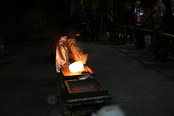 Photograph of a figure pouring the molten gold out of the crucible.