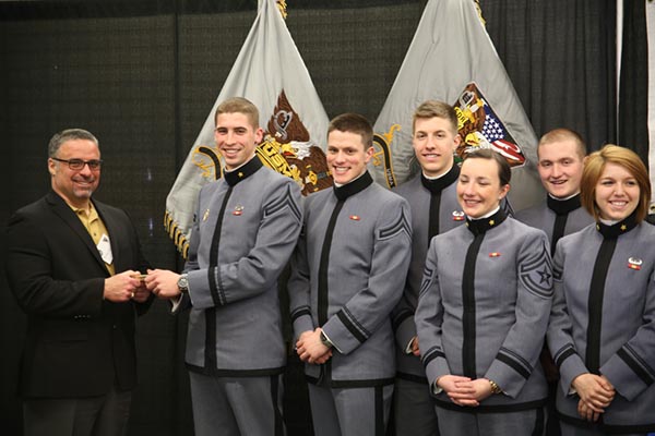Photograph of cadets posing. One of them is holding an object with a man in a black suit.