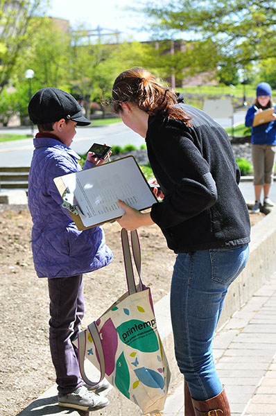 Photograph of a woman with a clipboard and bag speaking to a child.