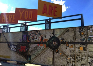 Satellite photo on a sign with smaller signs above it reading: "Here you are"