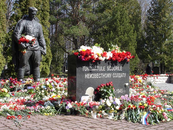 Bronze soldier statue overlooking flowers laying around a memorial.