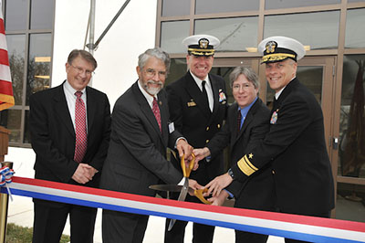 Photograph of a group of people standing around over-sized scissors and a ribbon.