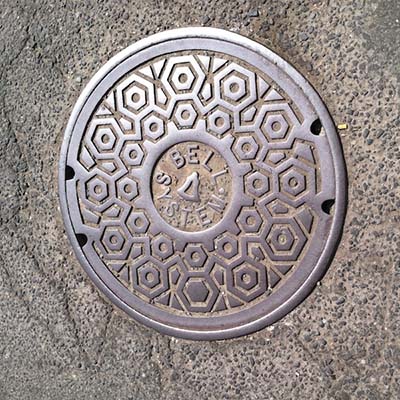 Photograph of a man hole cover with the Bell Systems logo in the center.