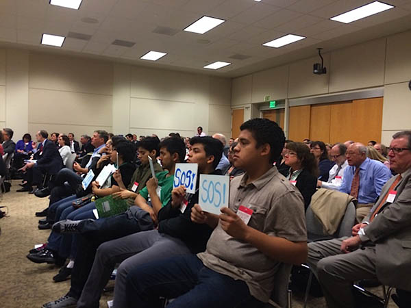 In the front row of the audience, high school students from communities around the Salton Sea hold up signs readings “SOS!” and “Save Our Sea!,” positioning the signs so that Water Resources Control Board members can see them.