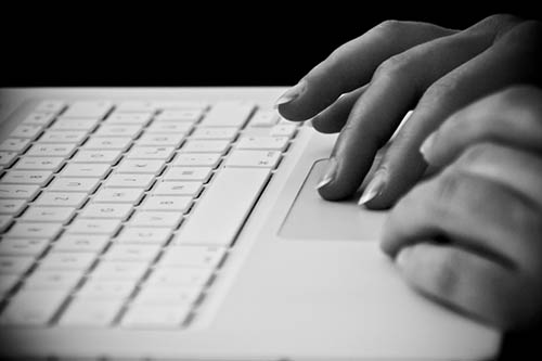 A black and white photograph of hands using a touchpad on a laptop keyboard.
