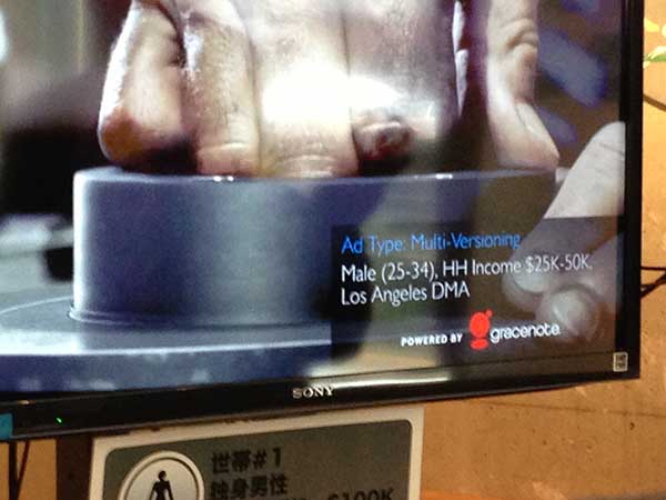 Photograph of a screen displaying a close up a hand that says "Ad type: Multi-versioning Male (25-34), HH income $25k-50k, Los Angeles DMA Powered by gracenote".