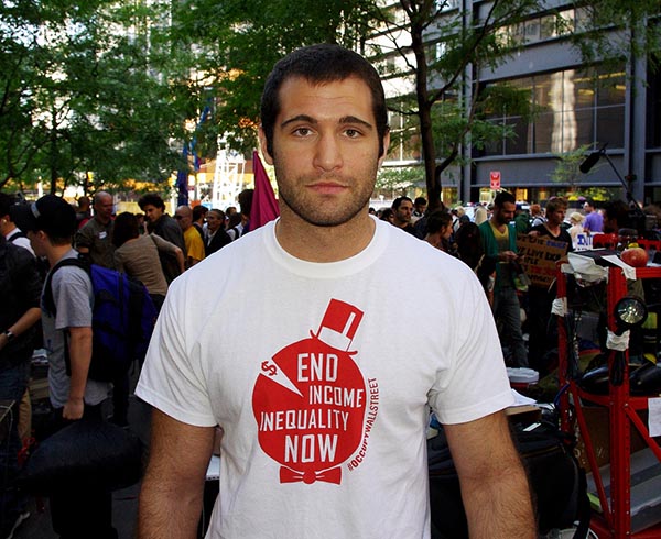 Man in a "End Income Inequality Now" T-Shirt facing the camera with crowd in the background.