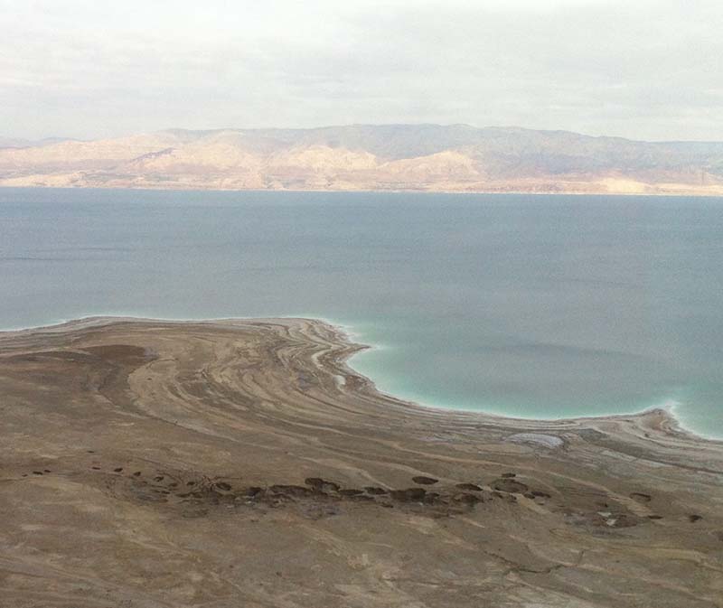 Distant view of multiple sinkholes near the Dead Sea, with the water and far shore in the background.