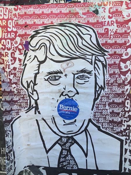 Street art of Donald Trump that has had a Bernie sticker placed over his mouth.