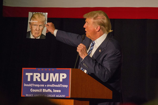 Photograph of Donald Trump holding up a Times magazine cover with his face on it.