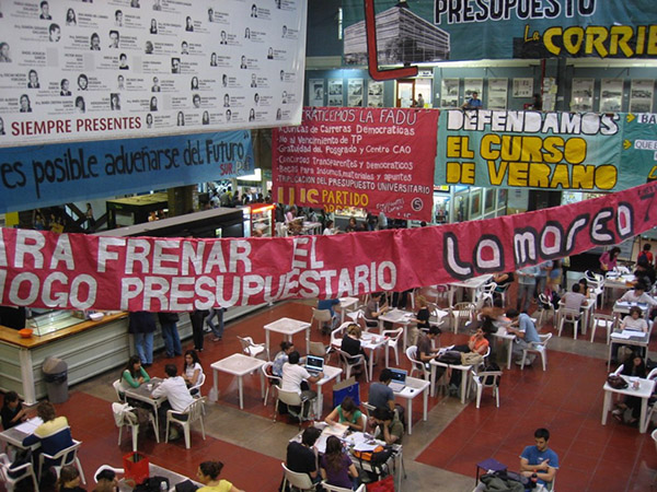 Photograph of a room filled with people sitting at tables with many banners above them.