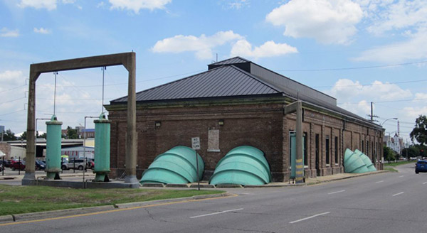 Photograph of a brick building with large green pipes coming out of the sides.