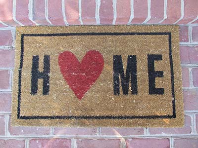 Photograph of a welcome mat that says home with a heart instead of an o.