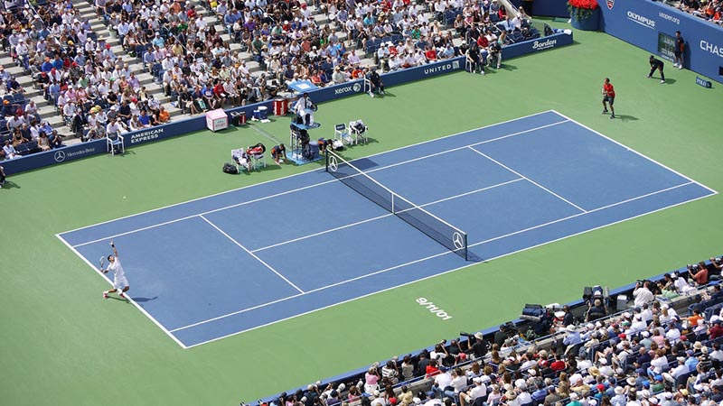 A picture of two men playing tennis, taken from up in the stands. Specifically, Djokovic serves to Federer in the US Open semifinal.