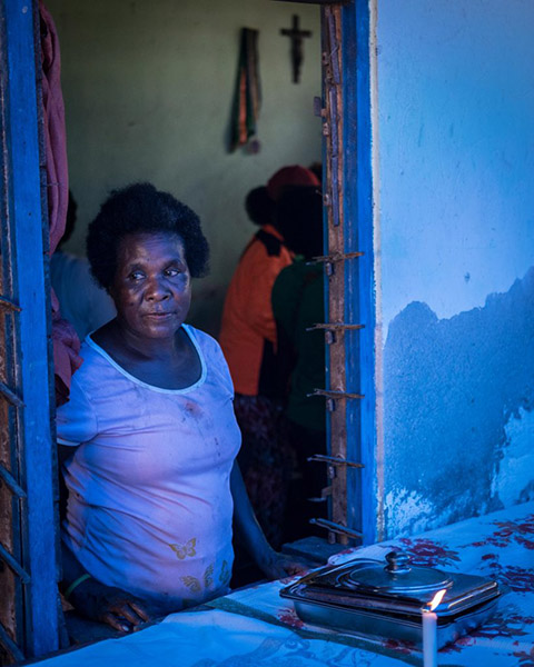 Photograph of a woman looking through an opening in the wall. She is lit by a blue light.