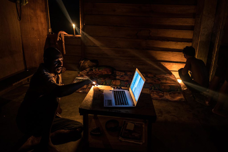 Photograph of a man using a laptop in a dark room.