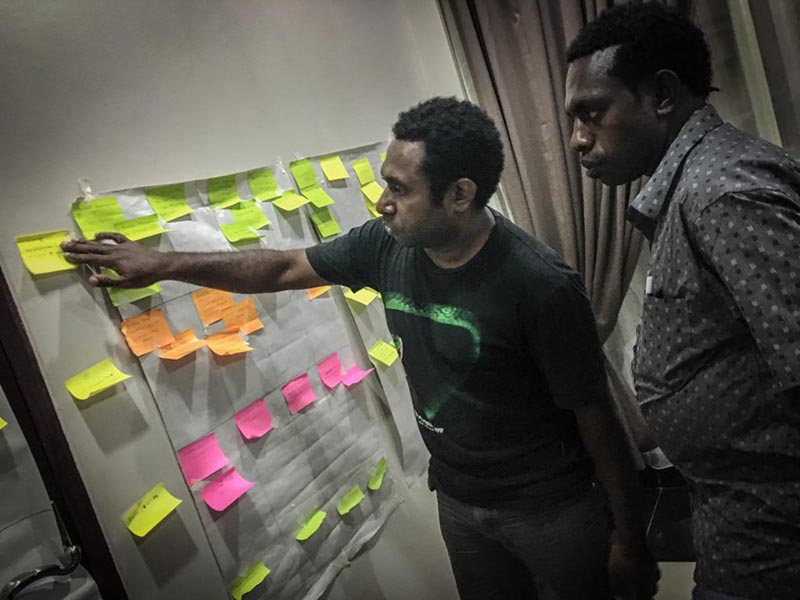 Two men looking at a board filled with sticky notes.