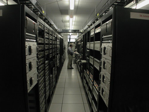 A photograph of a man working at a terminal in the middle of a row of server racks in a data center.