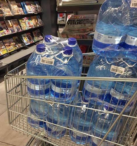 Photograph of a shopping cart overflowing with shrink wrapped large water bottles.