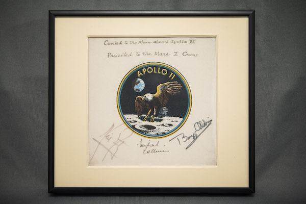 Photograph of a framed patch mounted on paper that has signatures on it.