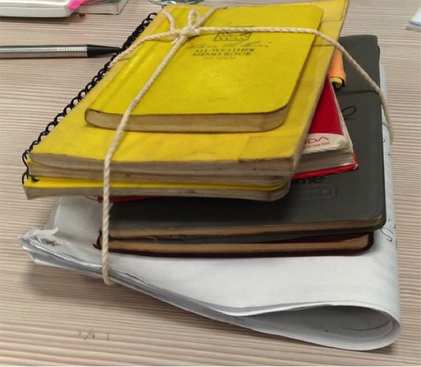 Photograph of yellow, red and grey journals tied together with twine along with folded paper.