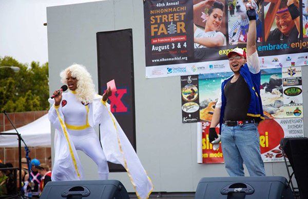 A drag queen in a Storm (X-Men) costume and a person in a Pokemon costume stand on a stage.