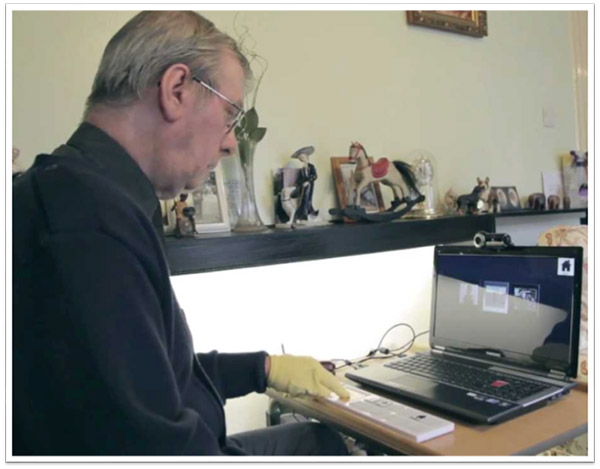 An older man sits in front of a laptop, pressing a large button on an adapted keyboard