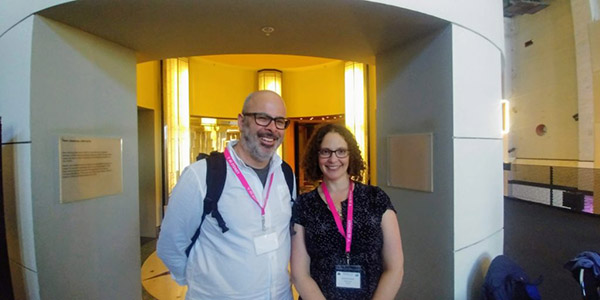 Photograph of two people posing for the camera and wearing pink conference badges.