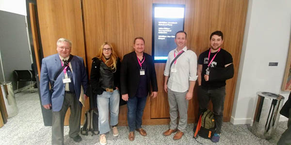 A photograph of five people wearing pink conference badges posing for the photo.