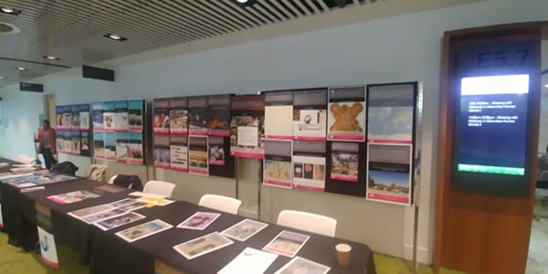 Photograph of a wall display of images with a long table with more images on it in front of it.