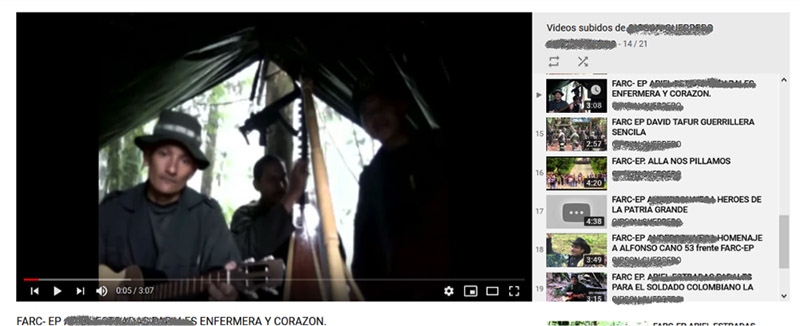 A screen capture of a YouTube video of Farc music. The still shows a man a gray shirt and gray broad rimmed hat, in a tent, and one other person the background.