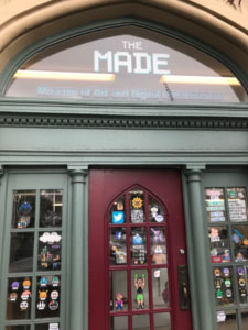 Photograph of a front door with the windows covered in stickers. Above the door a window has the sign "The Made: Museum of Art and Digital Entertainment"