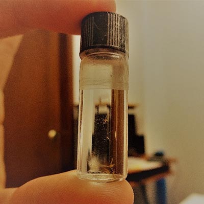 Photograph of a small glass vial held between a thumb and finger.