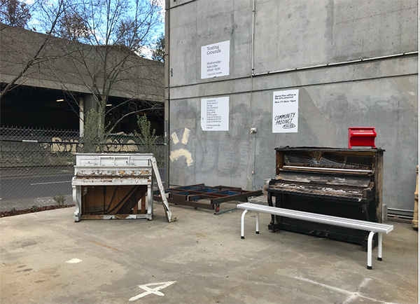 Photograph of two pianos with substantial visible damage outside beside a concrete wall.