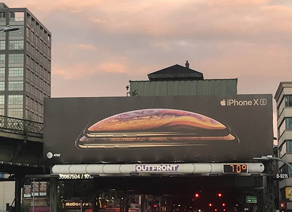 Photograph of a billboard for the iPhone with sunset sky and city in the background.