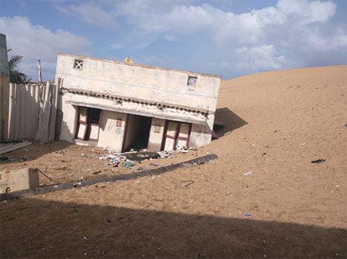 A whitewashed concrete building sinking into sand.