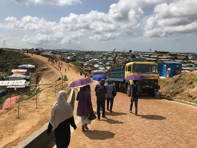 refugees walking on a dirt road with truck in the background