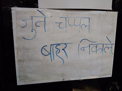 A sign written in Hindi reads "please leave your shoes outside."