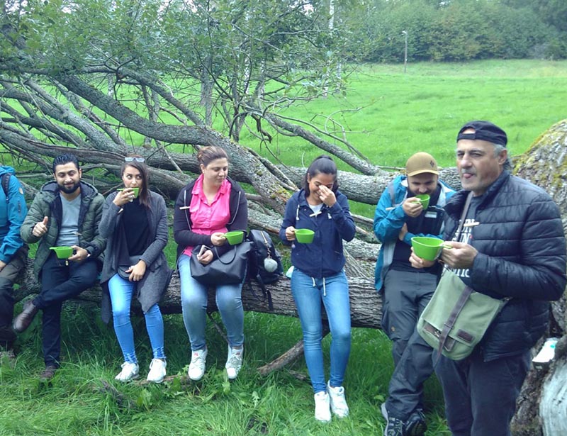 NBI participants sit on a large fallen log in a green field while taking their coffee break during an NBI.
