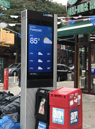 LinkNYC electronic kiosk surrounded by garbage bags