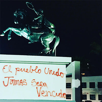 A statue of a Spanish conquistador sprayed with red graffiti reading "the people united will never be defeated."