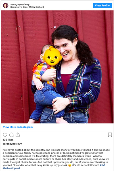 An Instagram photo altered to hide a child's face. A woman is posing holding a small child. The child's face is hidden behind a baby face emoji.