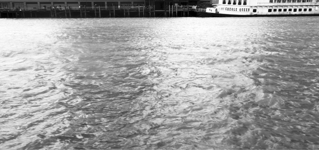 Black and white photograph of the Mississippi River, taken aboard a tourist replica of a steam boat, the Mississippi River Queen.