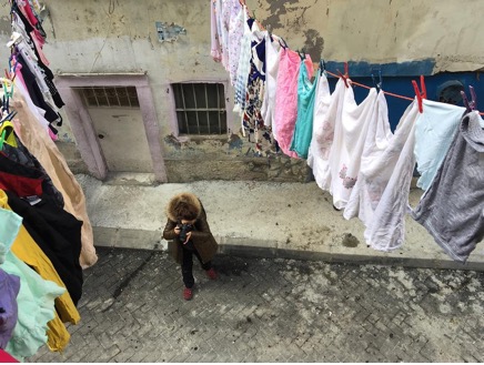 The image taken from the second floor showing a photographer standing under clothes lines with clean colorful laundry and taking a picture of something.