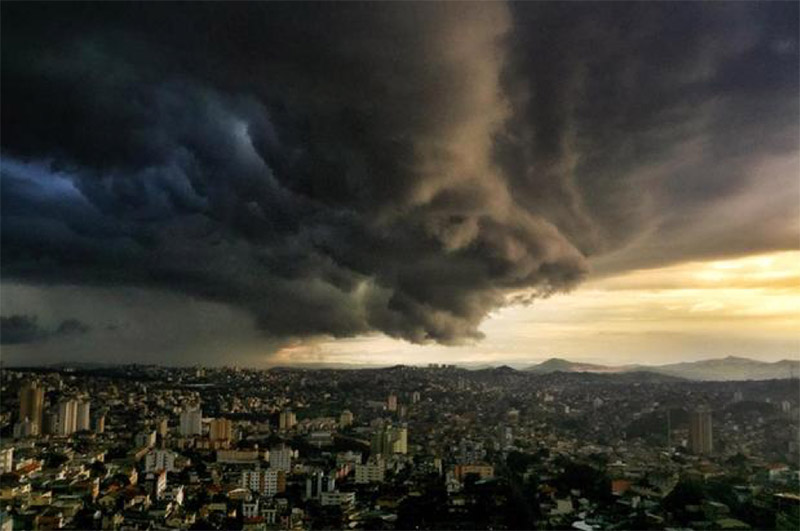 Dark, ominous storm clouds hover over a dense city with mountains in the background.