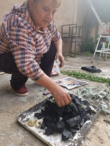 Una señora prende carbón en un patio para ch'allar una casa.