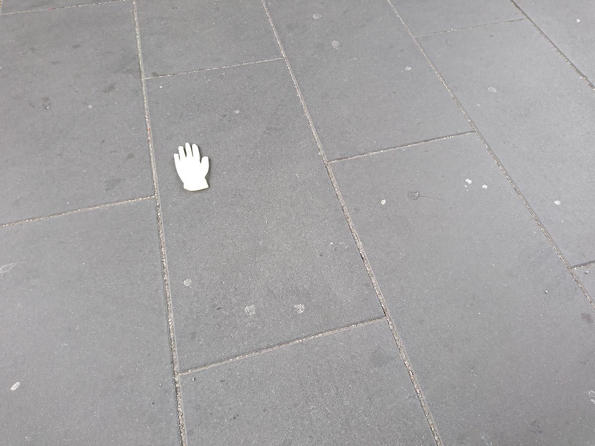 A single latex medical glove lays discarded on grey concrete. The white glove is small in the image but stands out.