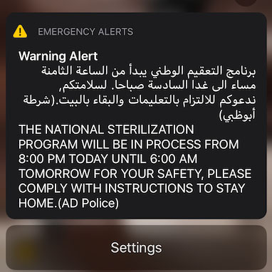 An emergency alert on a cell phone screen in Arabic and English reading "The national sertilization program will be in process from 8:00 PM today until 6:00 AM tomorrow for your safety, please comply with instructions to stay home. (AD Police)